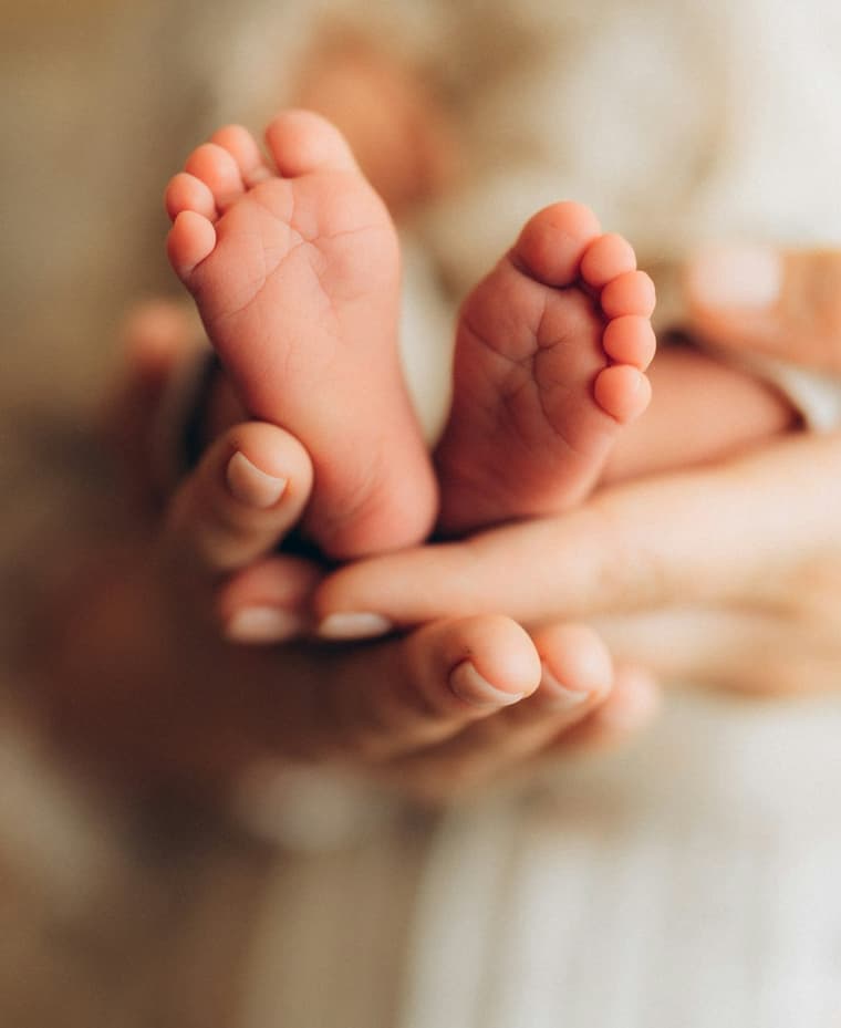 Mãos de adulto segurando os pezinhos de um bebê